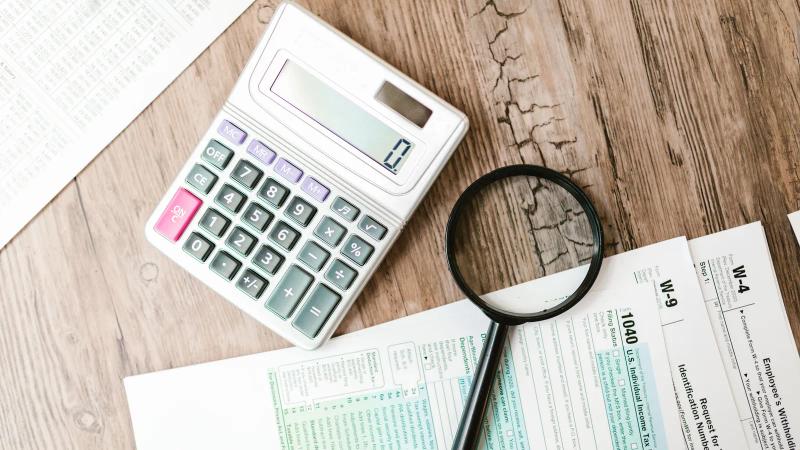 Formularios oficiales sobre una mesa de madera con una calculadora y una lupa encima de las cifras impresas
