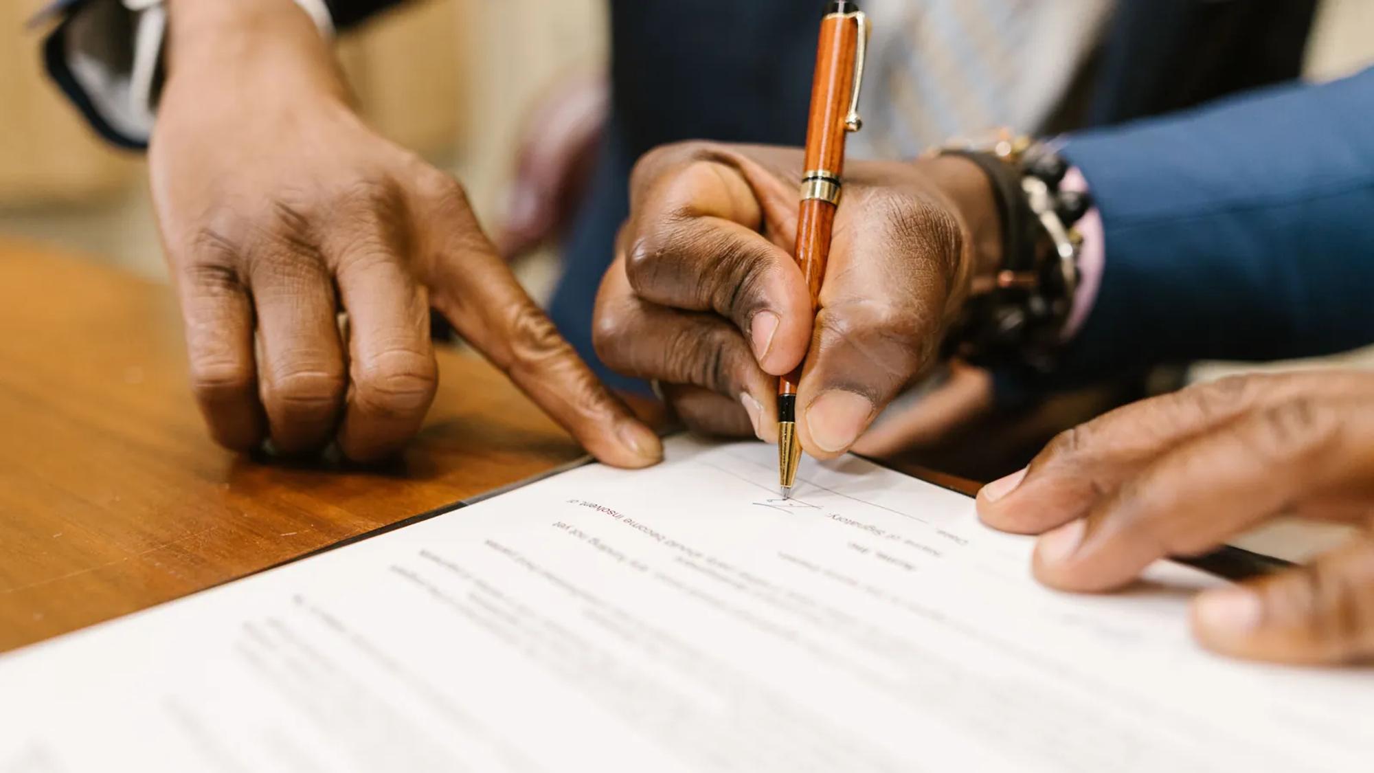 A hand writing on a printed contract in close-up, with the terms of the agreement visible under the pen.