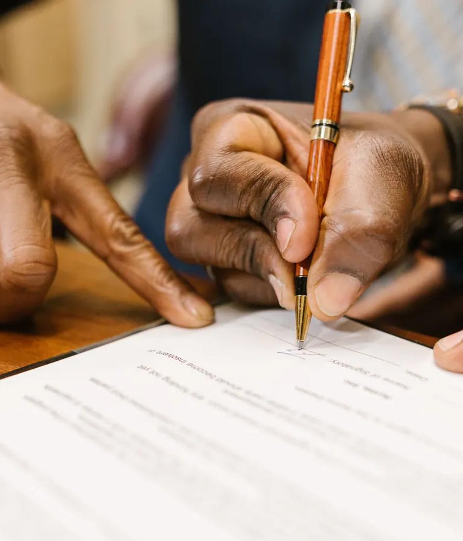 A hand writing on a printed contract in close-up, with the terms of the agreement visible under the pen.