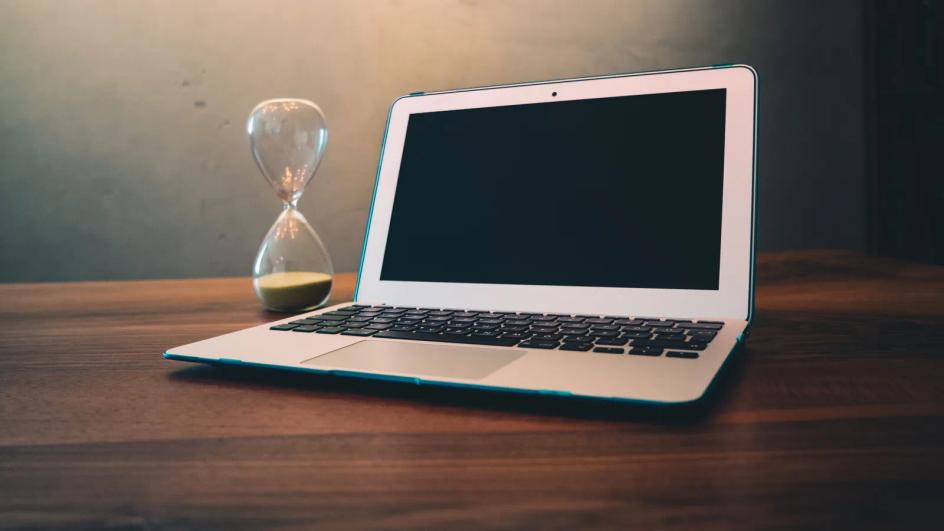 A laptop on a wooden desk beside an hourglass, the response clock running while nobody has been named as owner