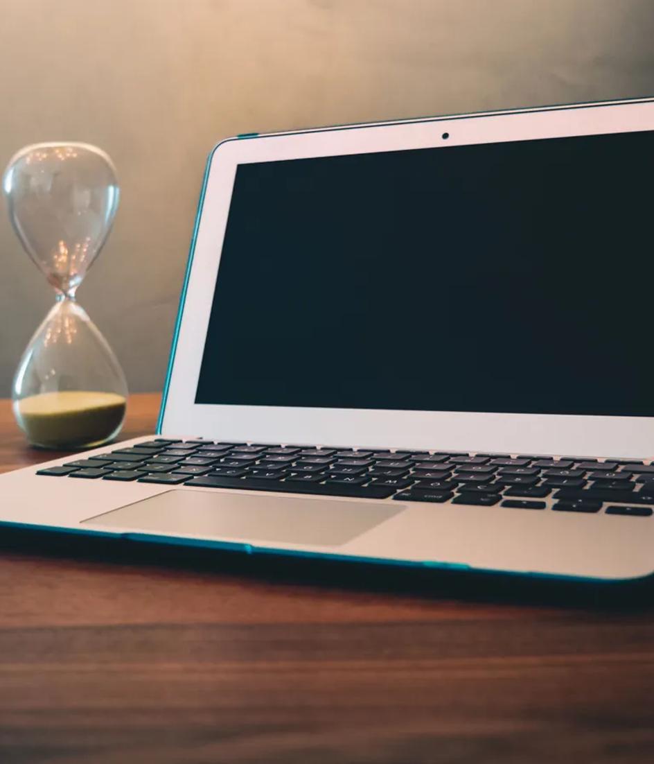 A laptop on a wooden desk beside an hourglass, the response clock running while nobody has been named as owner