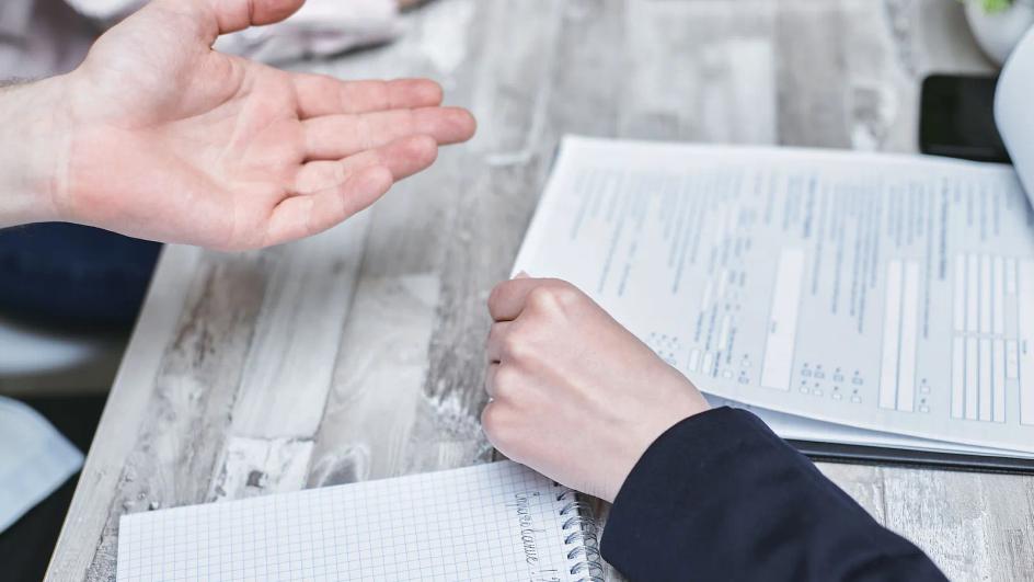 Documentos impresos sobre una mesa mientras dos personas los leen y anotan a mano durante una sesión de trabajo