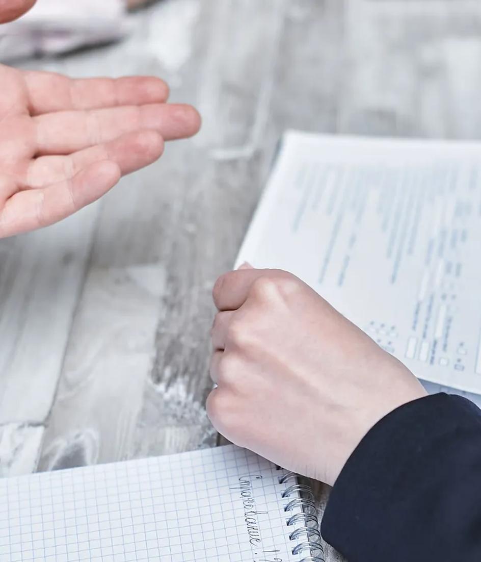 Printed documents spread across a desk while two people read them and take notes by hand during a working session