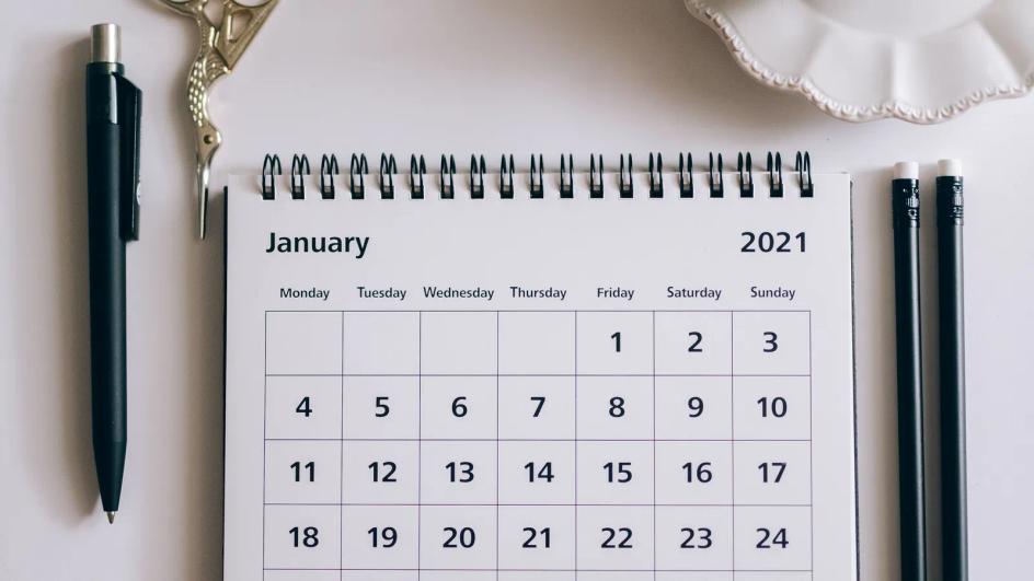 Desk calendar next to a pen, clips and scissors on a white surface, ready for dates to be marked
