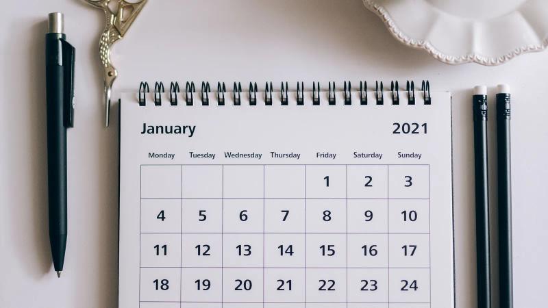 Desk calendar next to a pen, clips and scissors on a white surface, ready for dates to be marked