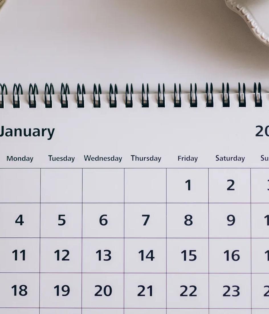 Desk calendar next to a pen, clips and scissors on a white surface, ready for dates to be marked