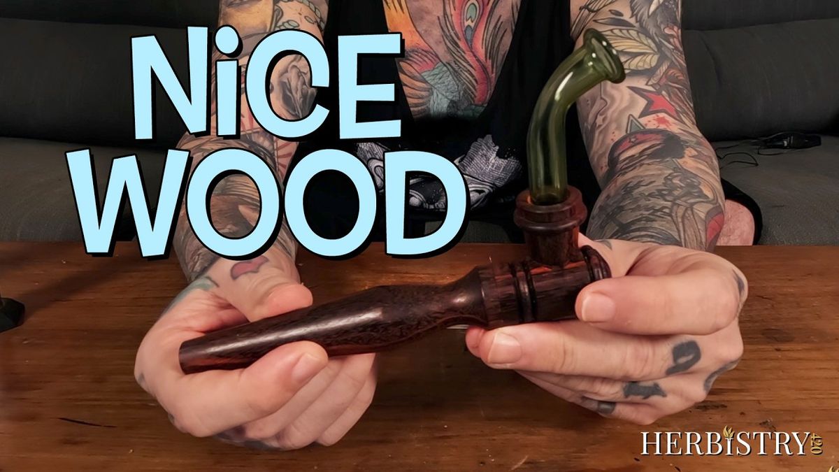 Hands holding the wooden Pipescents 2.0 vaporizer with a curved green glass mouthpiece attached