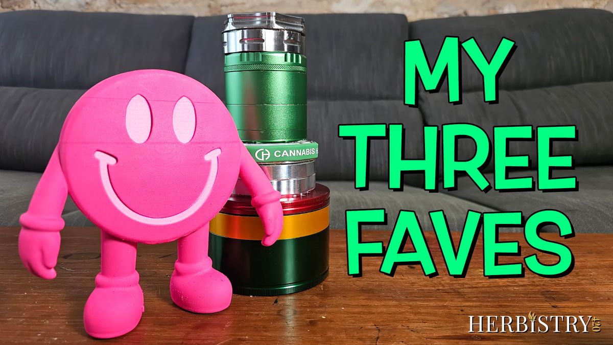 Pink smiley face grinder figure standing next to a stack of colorful grinders on a wooden table