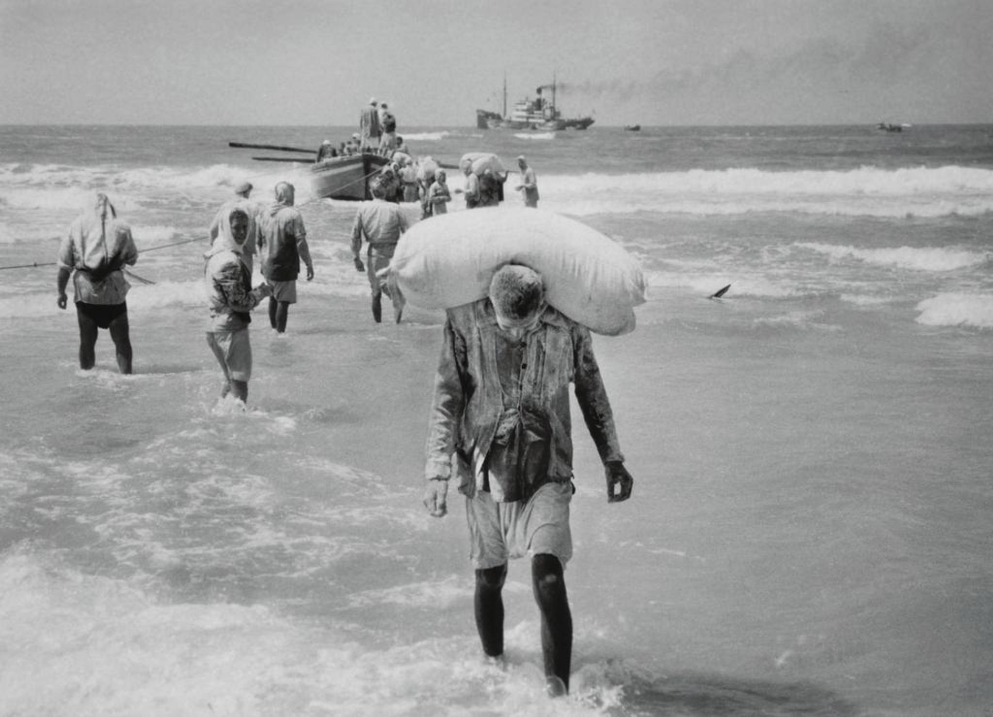 Palestinian refugees on the Gaza strip, carrying sacks of flour sent by UNRWA, from boat to shore.
