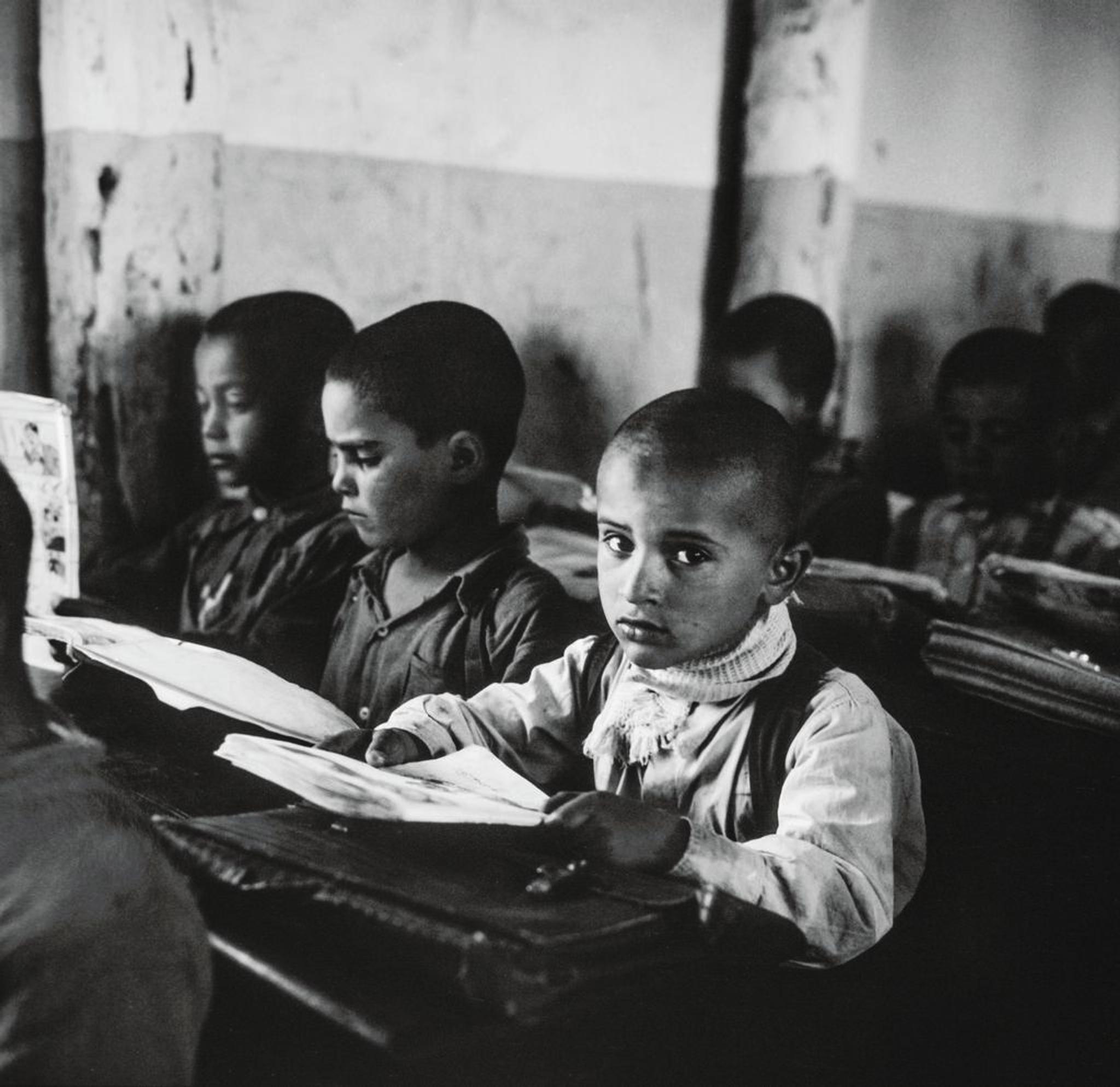 A group of boys in a classroom, open books on the desks, one boy is looking in the camera with a serious face
