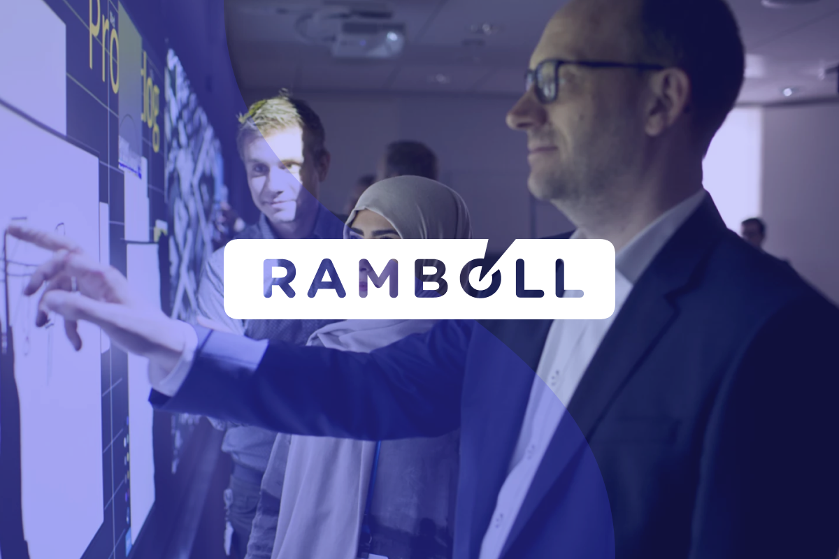 A picture of three people looking at a wall, with blue transparent overlay and the Rambøll logo over it