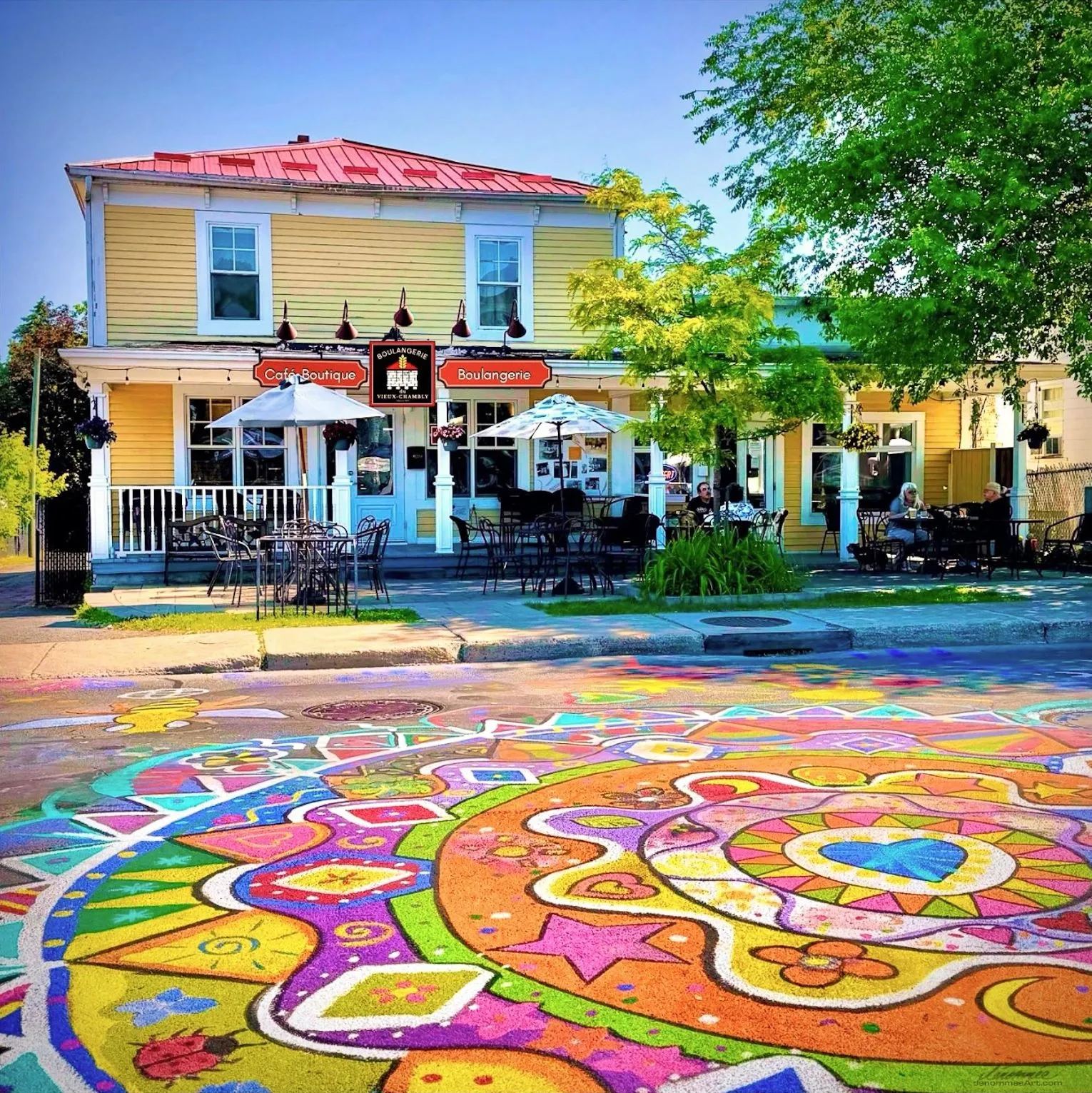 La Boulangerie du Vieux Chambly et sa terrasse, derrière un grand dessin de rue multicolore. Œuvre de Dénommée
