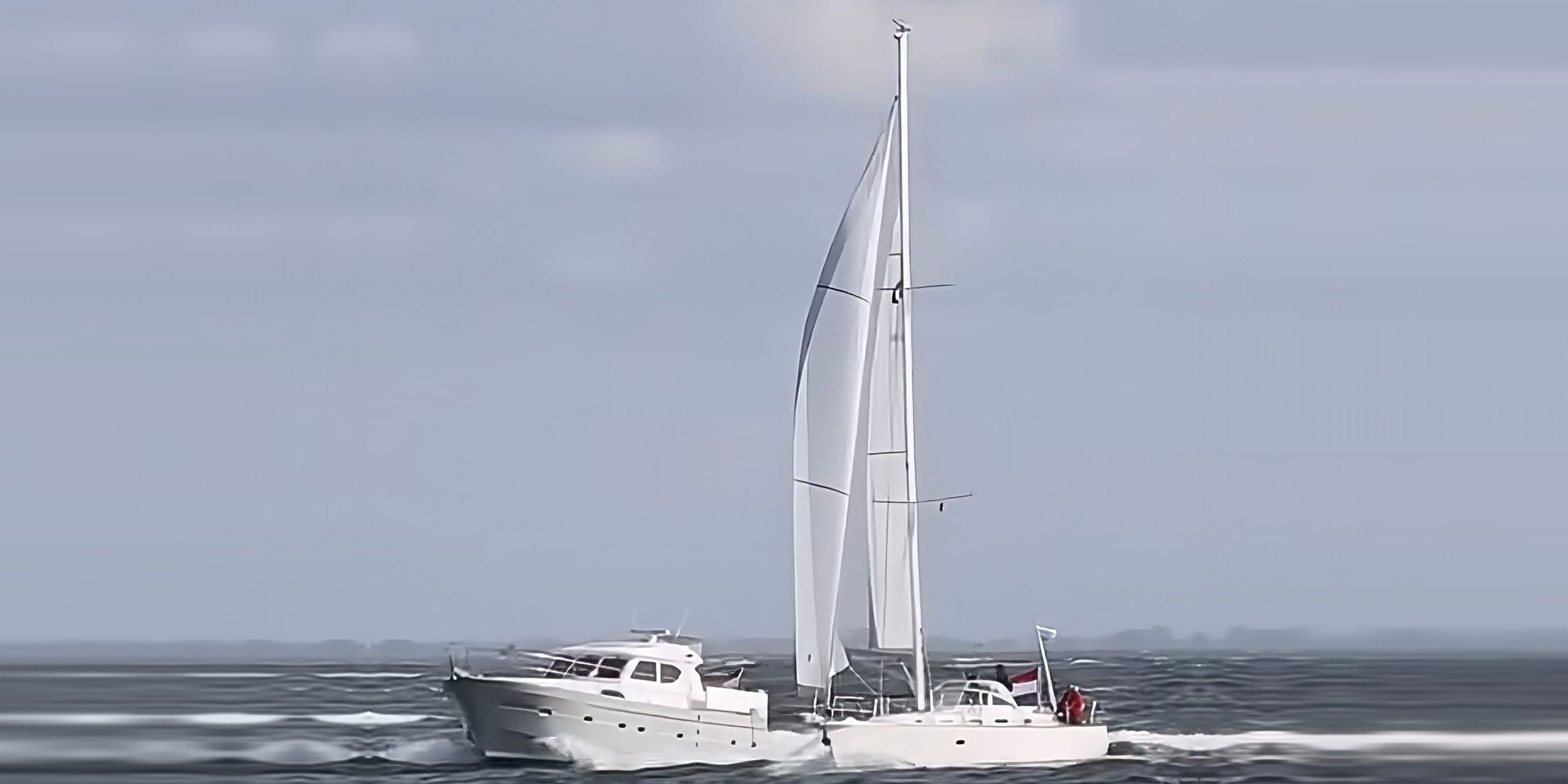 Een Elling-motorjacht en een zeiljacht onder vol zeil naast elkaar op woelig water