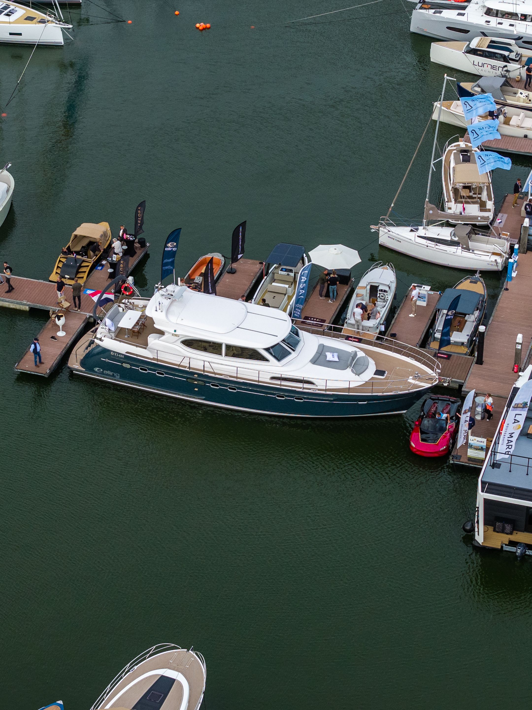Een luchtfoto van een Elling E6 met marineblauwe romp aan de steigers van HISWA te Water, tussen andere boten en bezoekers