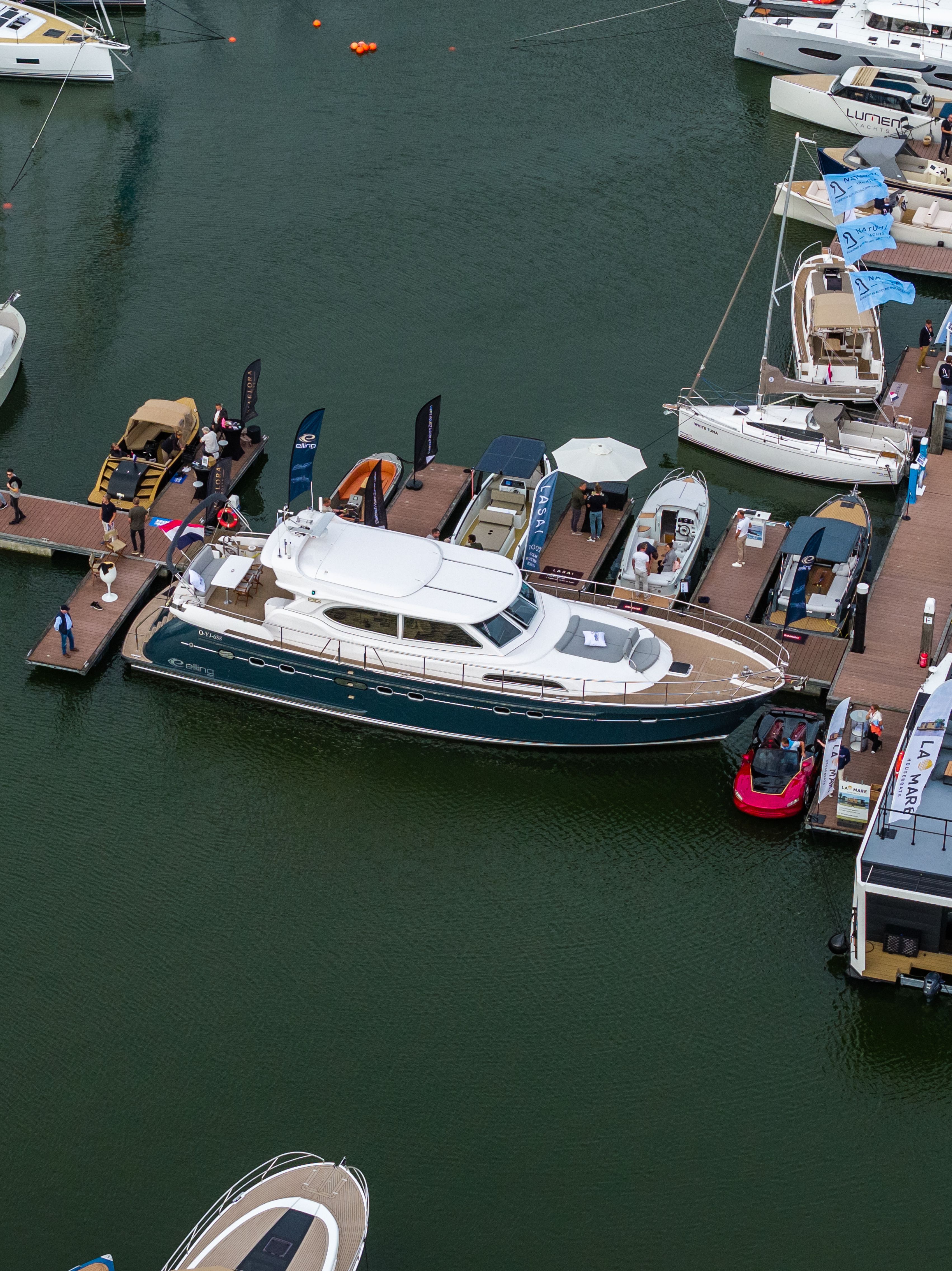 Een luchtfoto van een Elling E6 met marineblauwe romp aan de steigers van HISWA te Water, tussen andere boten en bezoekers