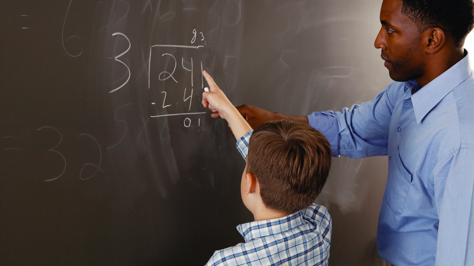 Math teacher assisting a student at the blackboard, solving a math problem together.