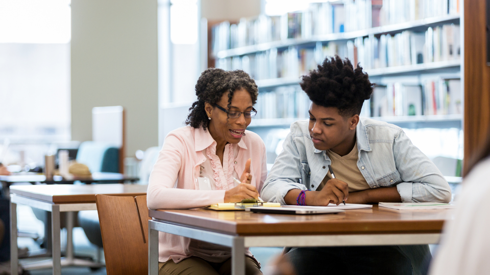 Student studying with a math tutor in a library setting.