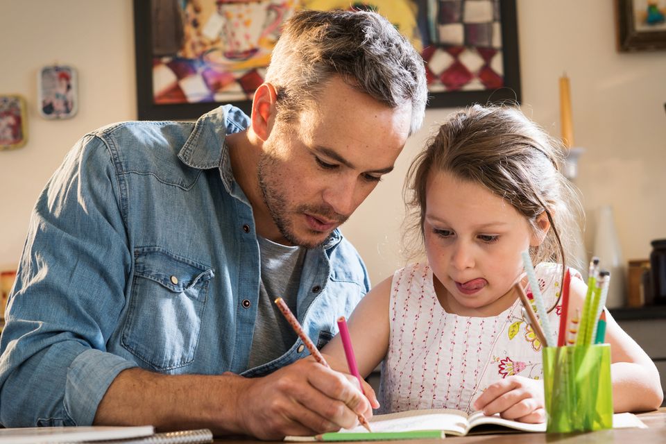 A father helps his young daughter with her homework.
