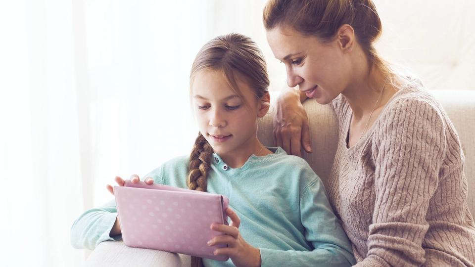 Mother watching daughter work on a tablet