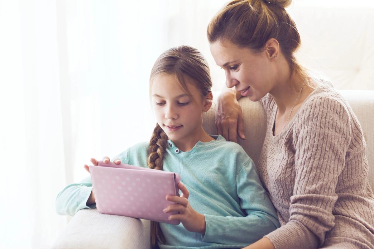 Mother watching daughter work on a tablet