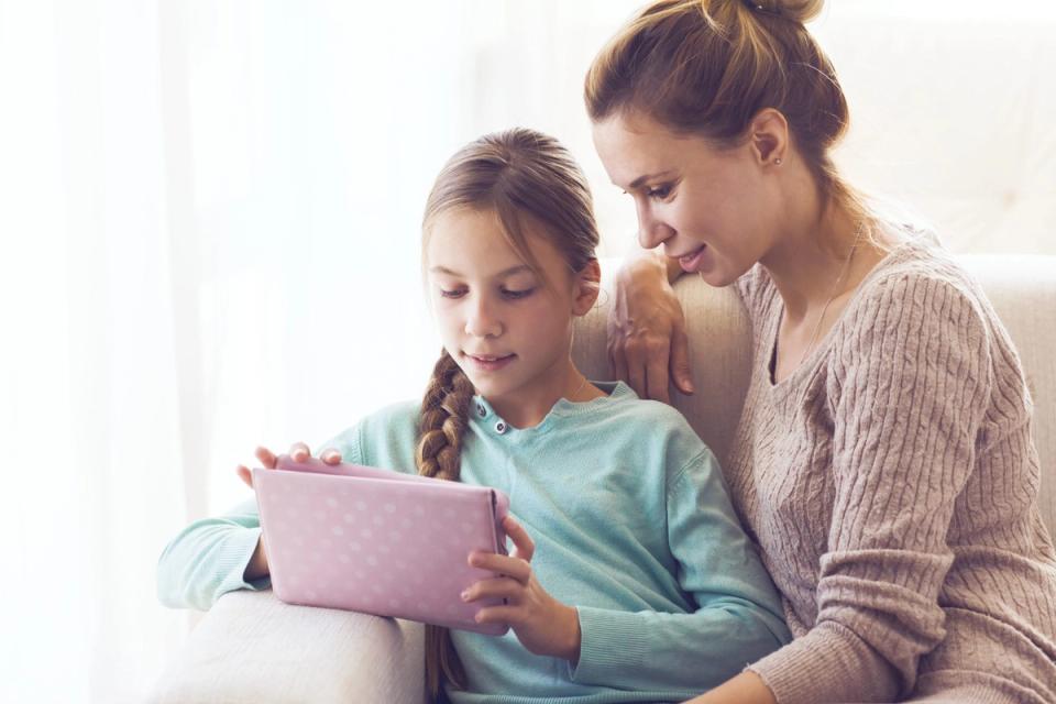 Mother watching daughter work on a tablet