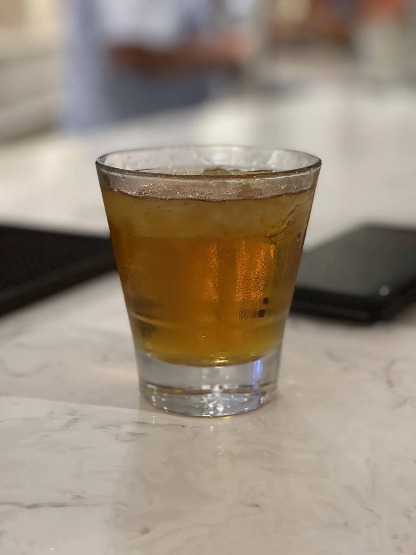 An amber drink with ice in a short glass on a marble counter