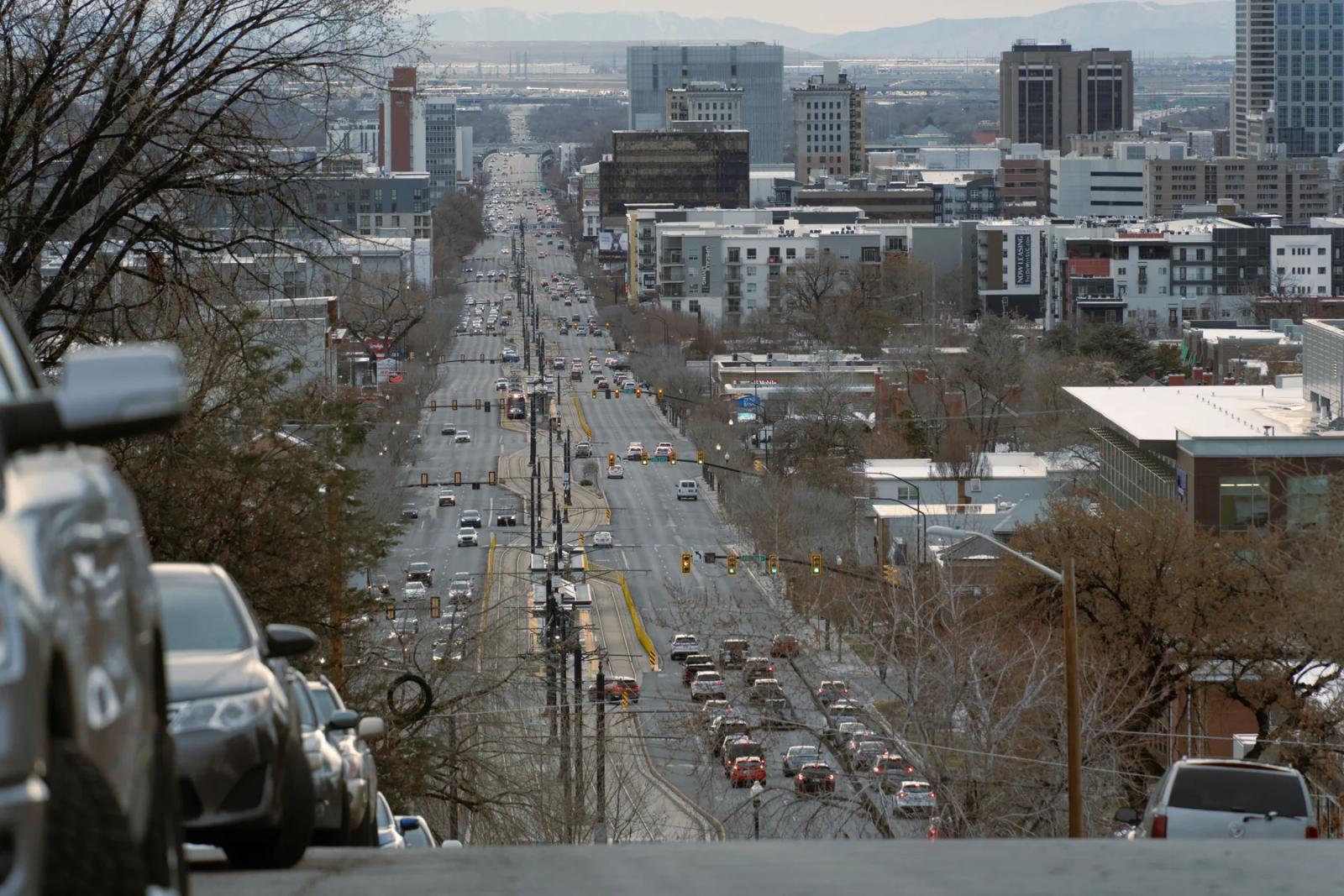 A Salt Lake City street lined with buildings, traffic lights and the Wasatch Mountains beyond