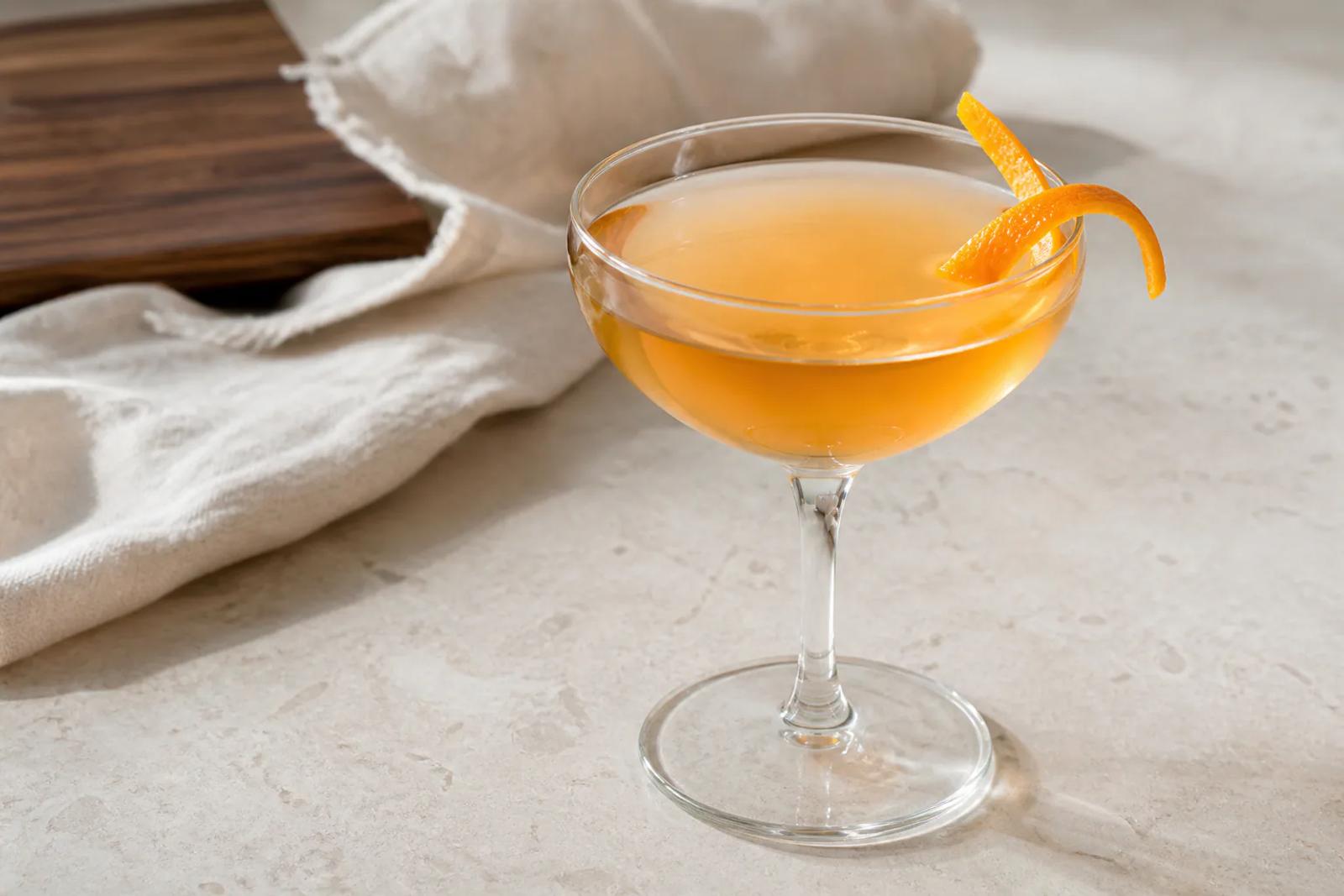 Amber-gold Sidecar in a clear coupe with an orange twist on pale stone.