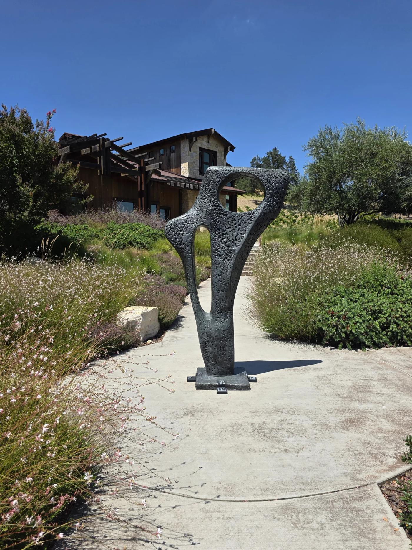 Dark metal sculpture surrounded by flowers outside a stone winery building at Halter Ranch