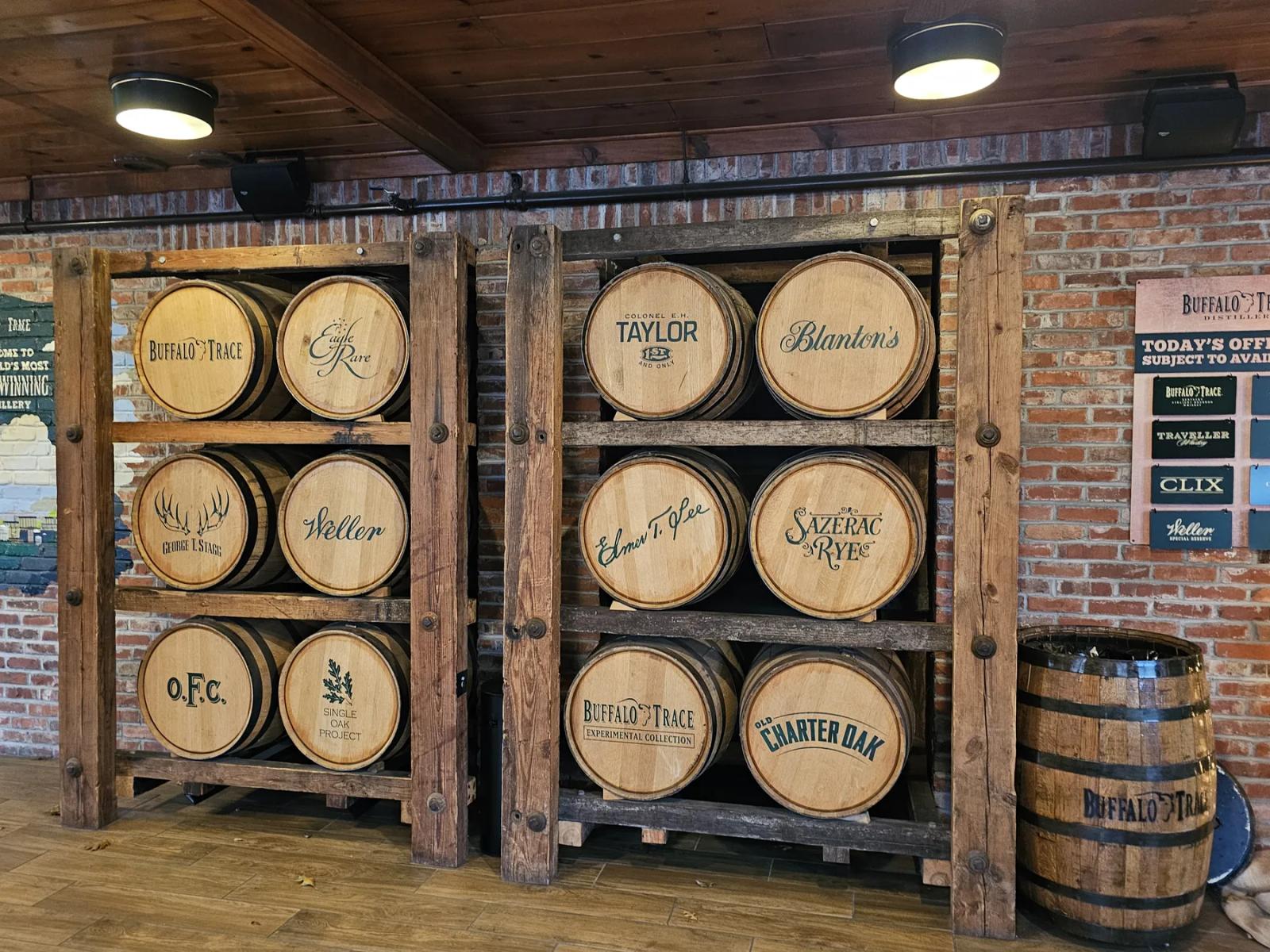 Labeled whiskey barrels displayed on wooden racks against a brick wall