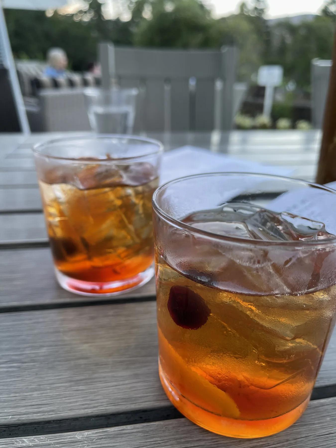 Two amber drinks served over ice in clear rocks glasses on an outdoor table