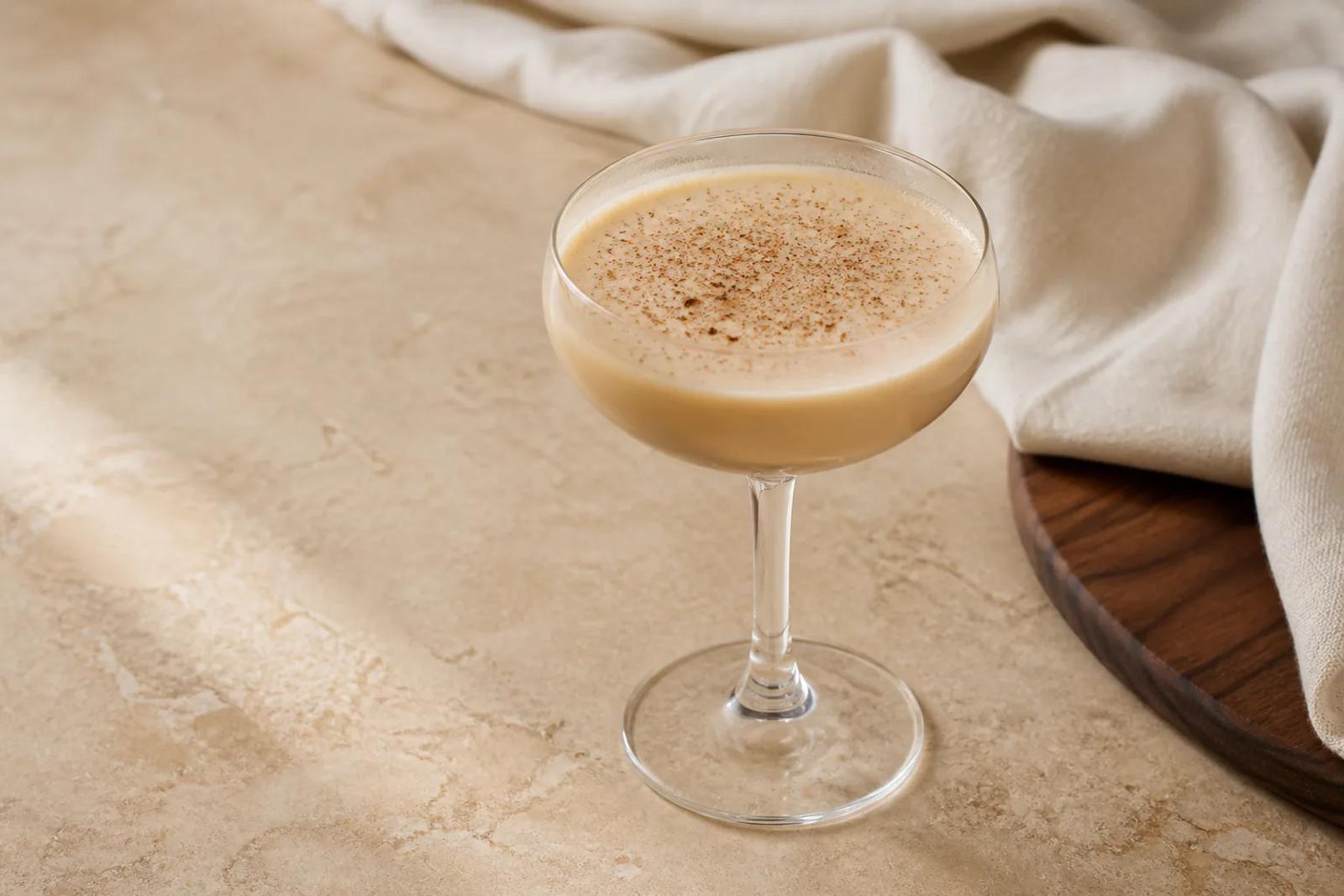 Creamy light-tan Brandy Flip in a small stemmed glass with a smooth surface and finely grated nutmeg.