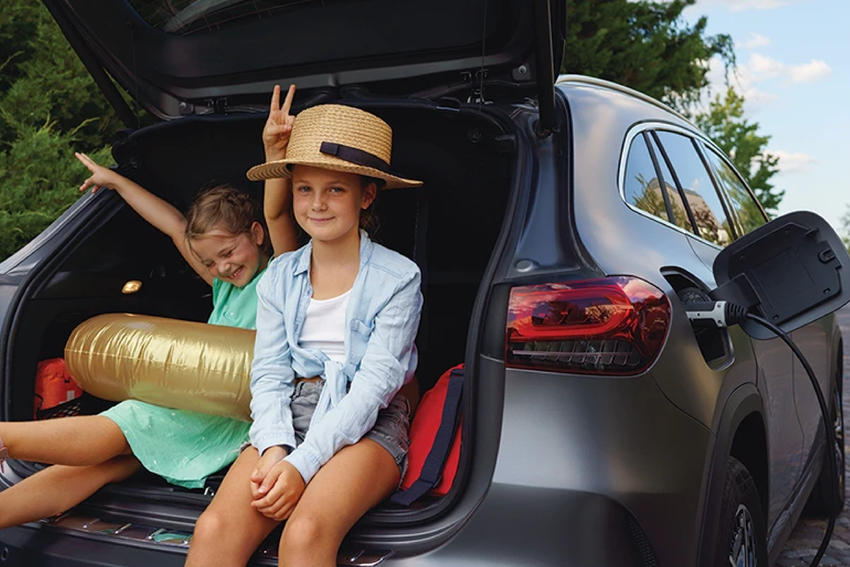 Two girls sitting in the boot of their family EV while it charges.