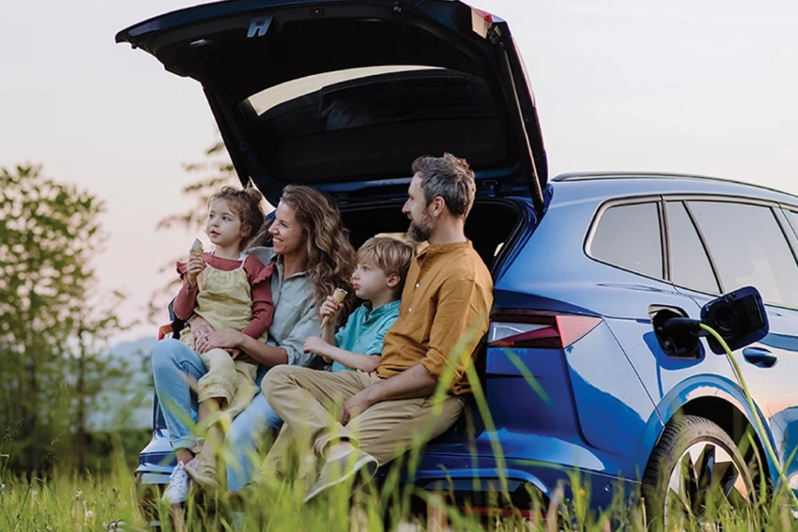 A family of four leaning on the open boot of their EV.