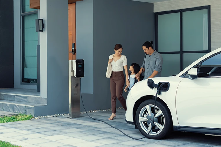 Family of three standing next to their charging EV at home.