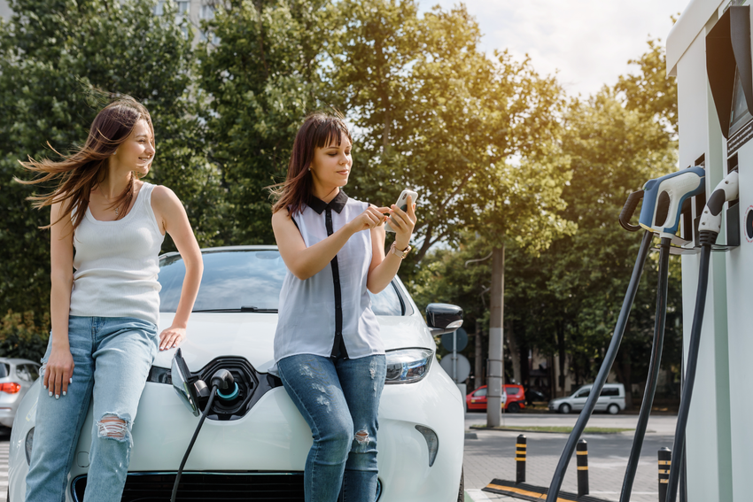 Two women sitting on the bonnet of their EV while it charges.