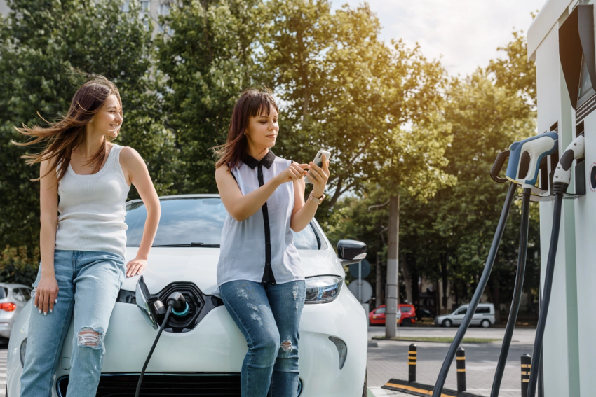 Two women sitting on the bonnet of their EV while it charges.