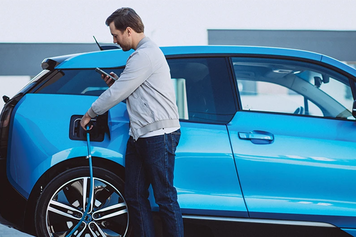 Person checking their phone and plugging a charger into their electric vehicle.