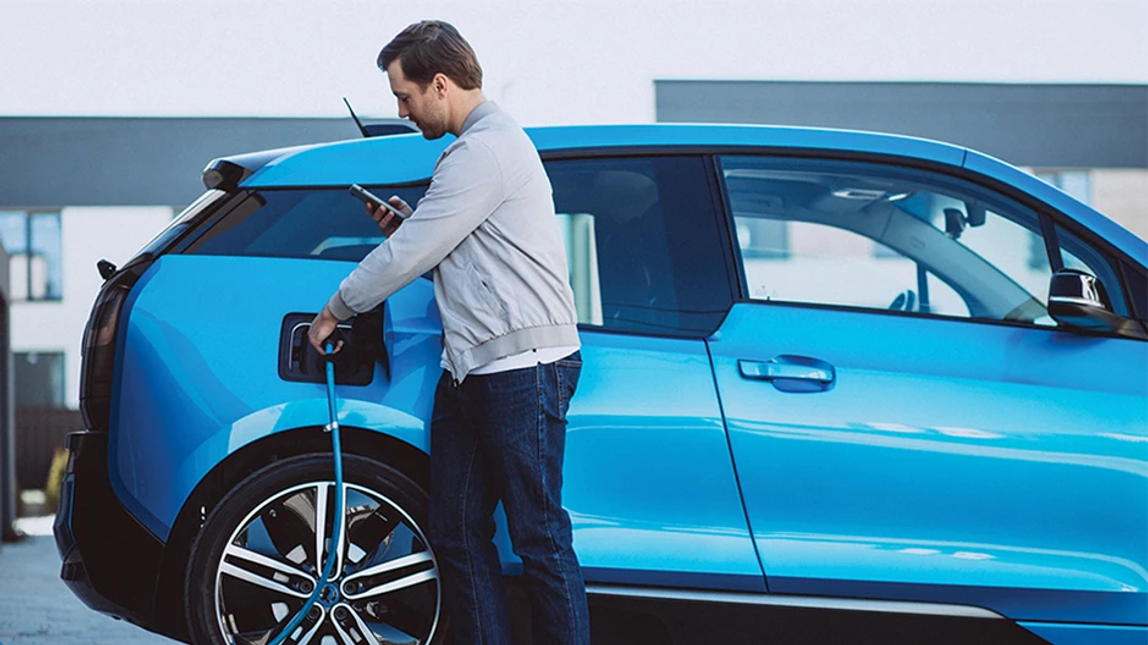 Person checking their phone and plugging a charger into their electric vehicle.