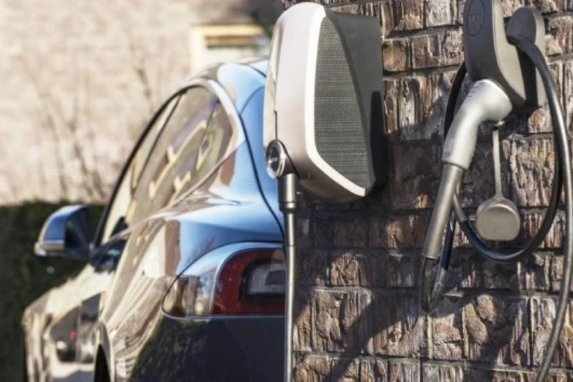 Cropped image showing the side of an electric vehicle and a wall mounted EV charger.