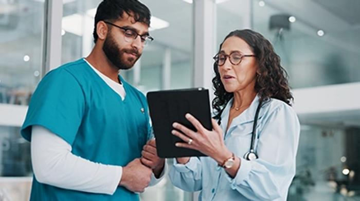 Two clinicians, one in surgical scrubs, reviewing training content on a tablet together in a hospital