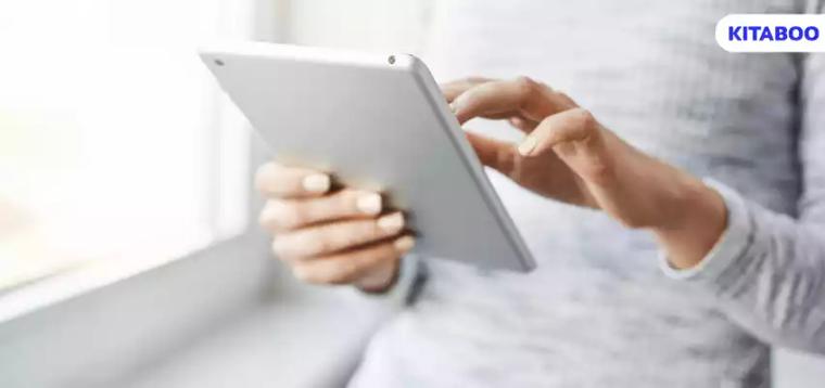Cropped shot of female student standing near window, touching screen of digital tablet,