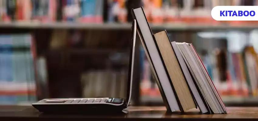 Laptop computer and book on workplace in library room