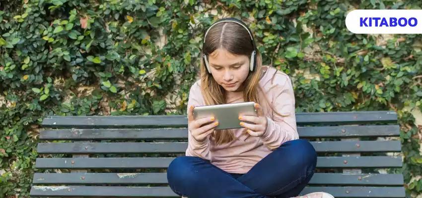 Girl sitting on bench wearing headphone using mobile phone in park