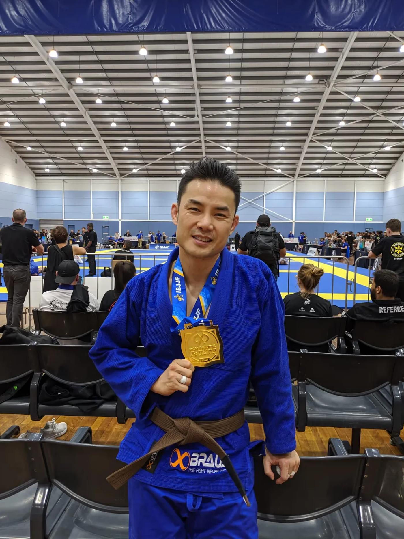 Jason Ng, Head Coach at Noble Grounds BJJ, holding a gold medal at a Brazilian Jiu Jitsu competition