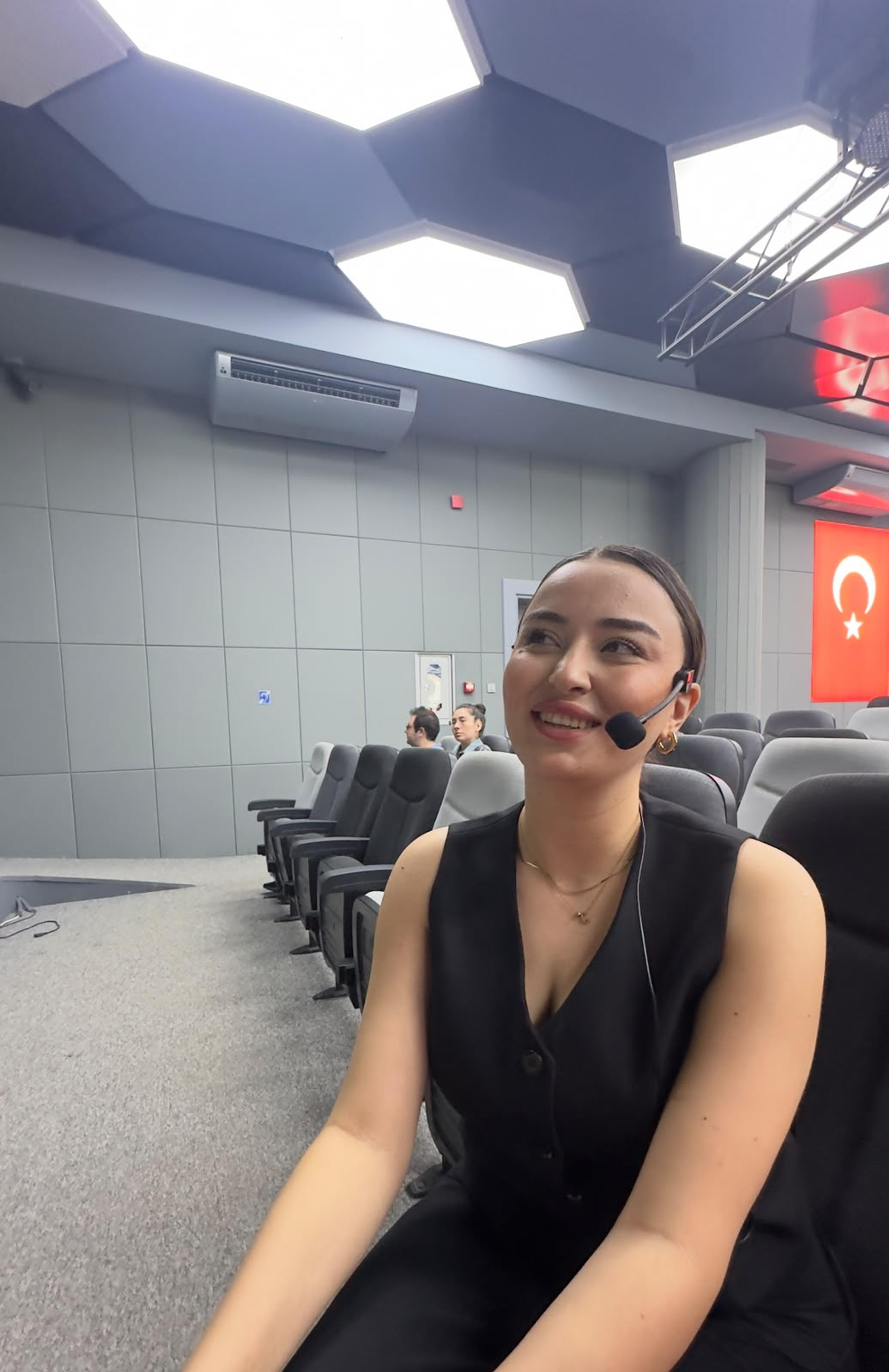 Ceren Höbek, yaka mikrofonuyla salonda, konuşmasından önce