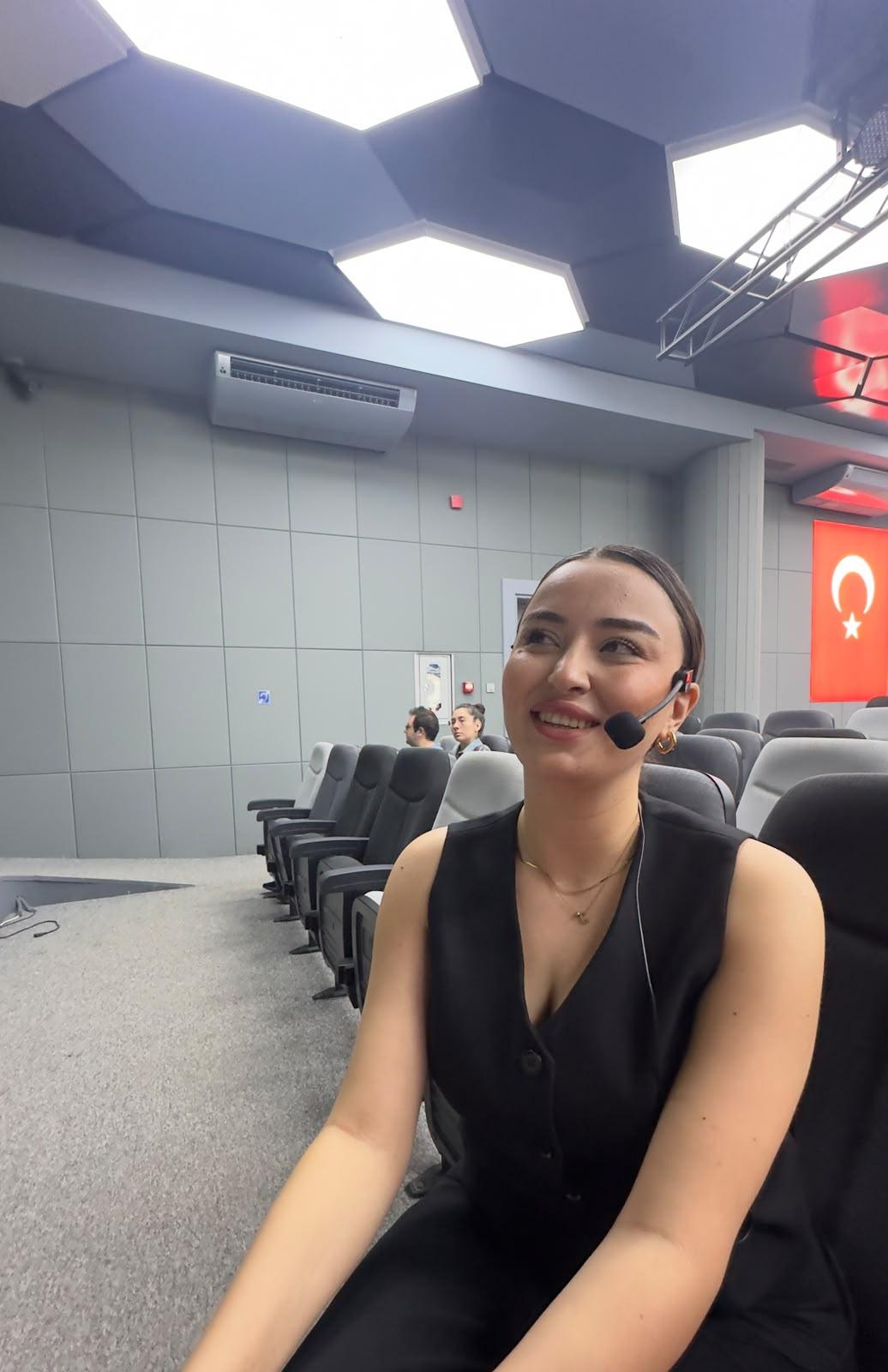 Ceren Höbek, yaka mikrofonuyla salonda, konuşmasından önce