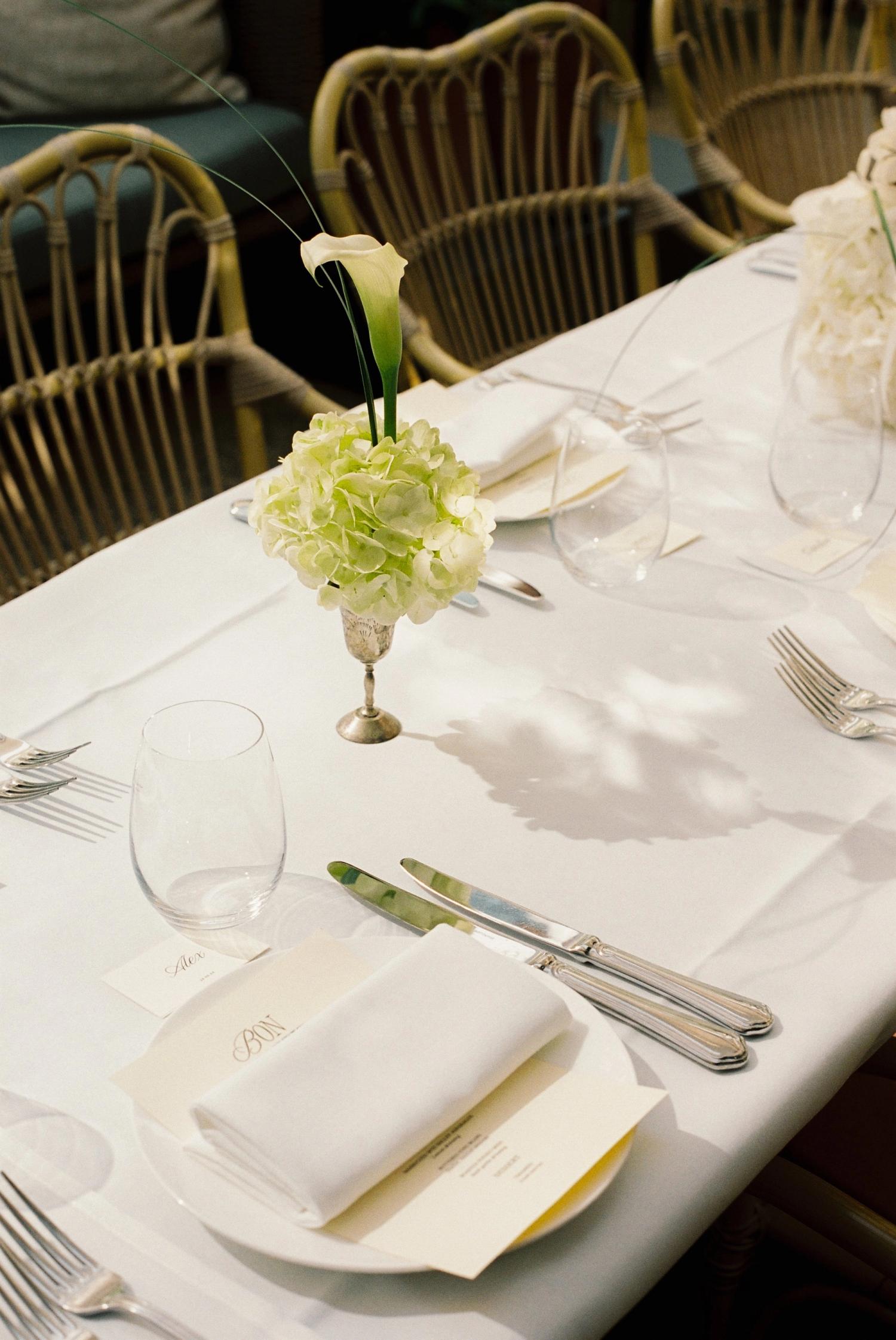 A laid wedding table, single calla lily in a glass, folded napkin and place card in low sun
