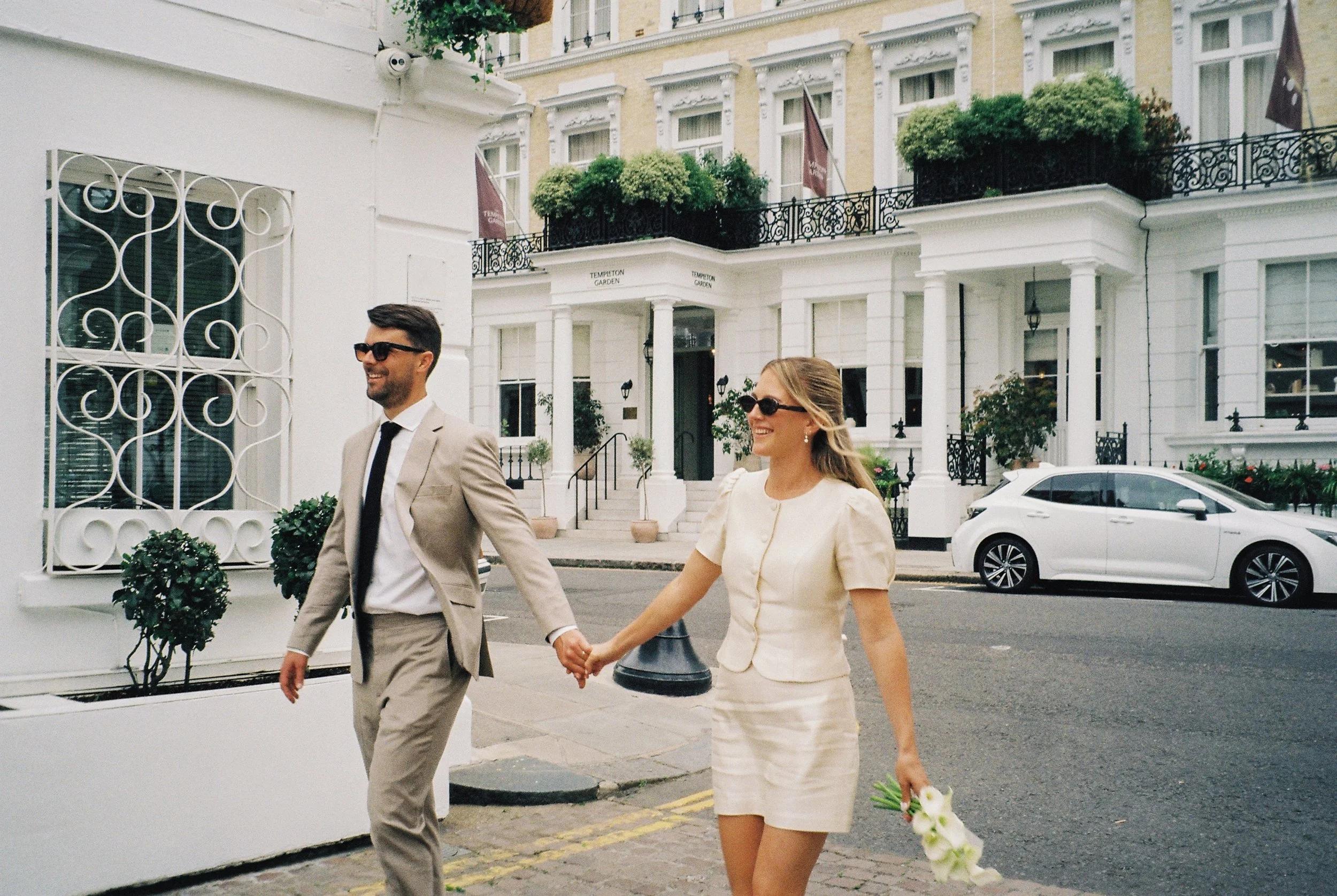 A couple walking a white stucco London street after their ceremony