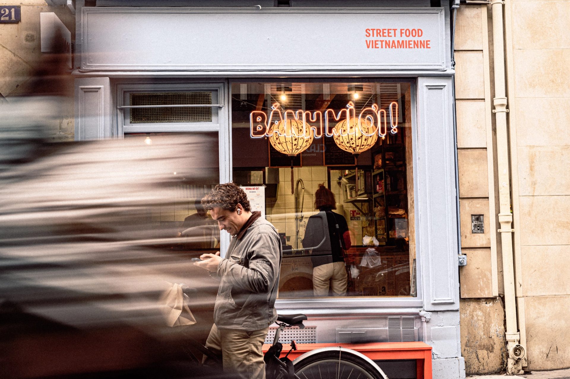 Devanture du restaurant Bánh Mì Oi! à Paris, avec son enseigne lumineuse et des passants dans la rue.